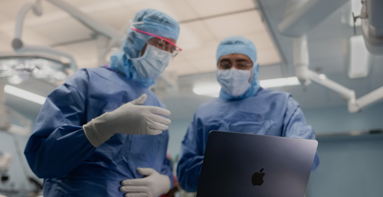 Two surgeons discussing something on the screen of a MacBook Pro in the OR.